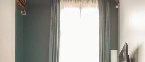 A bedroom with a bed, a television, a mirror, and a window with curtains.
