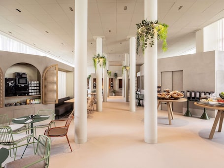 Un'ampia area interna con soffitti alti, colonne bianche e piante sospese.. ibis Styles Brugge Centrum