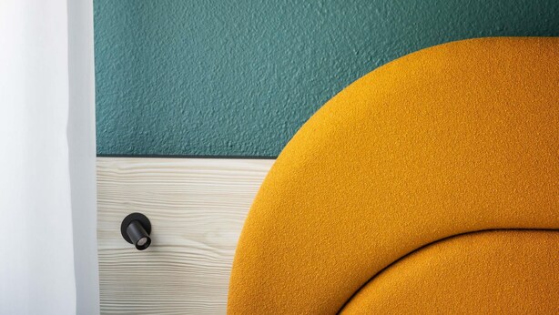 A room with a teal textured wall, a wooden floor, and a mustard-colored circular object. - ibis Styles Brugge Centrum (Bruges)