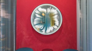 A room with a red wall, a circular mirror with a white frame, and two blue ottomans. - ibis Styles Brugge Centrum (Bruges)