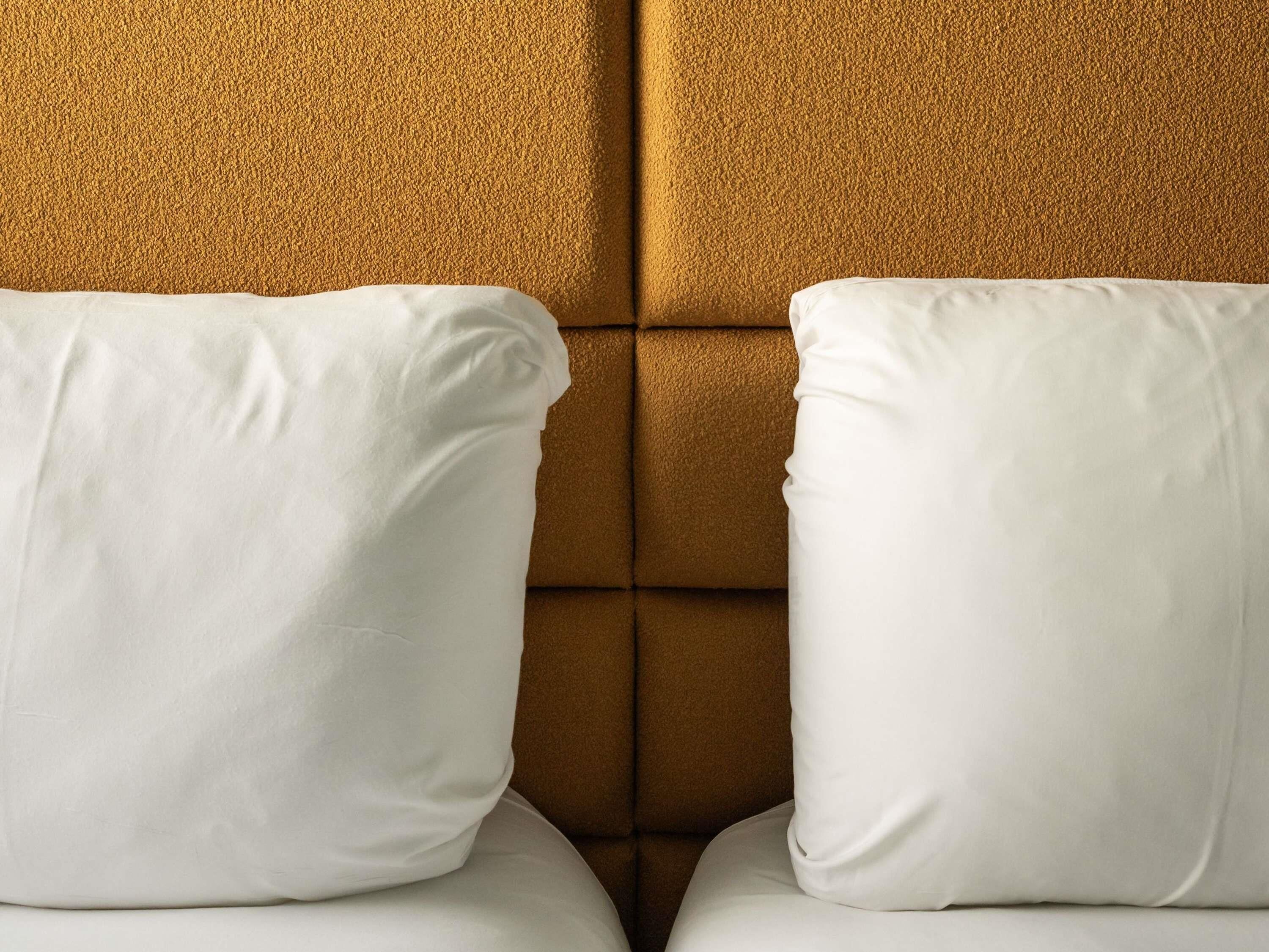 Dos almohadas blancas sobre una pared marrón texturizada.