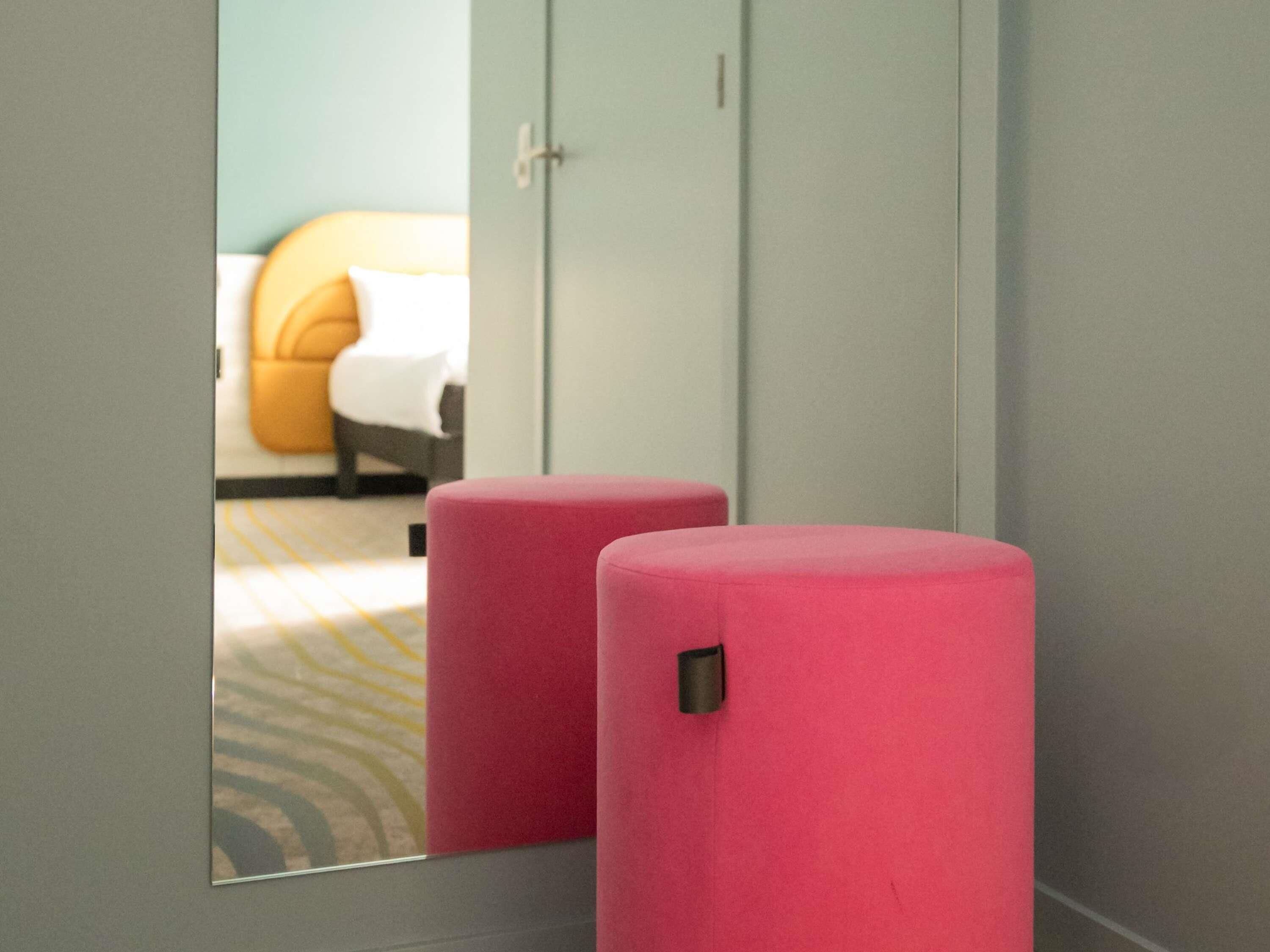 A room with a bed, a wardrobe, and two pink cylindrical stools.