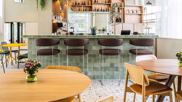 A modern bar area with a green-tiled counter, bar stools, and shelves stocked with bottles. - ibis Styles Brugge Centrum (Bruges)