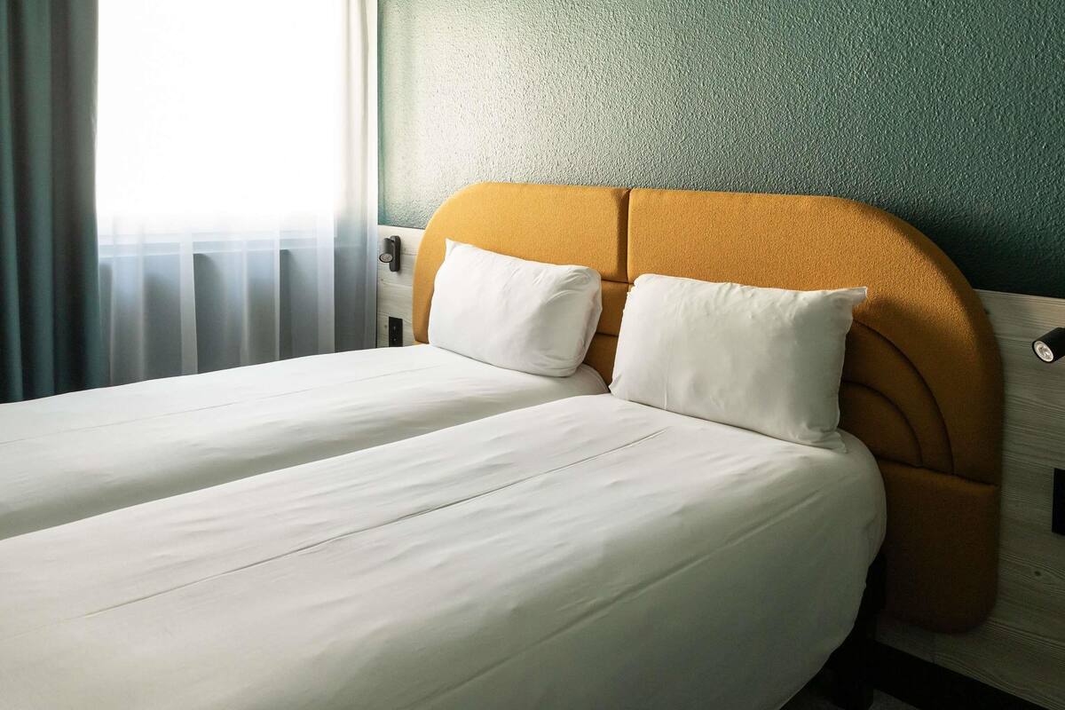A double bed with white linens, a mustard-colored headboard, and a textured green wall.