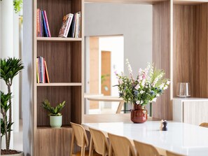 A modern dining area with a wooden bookshelf, a table, chairs, and a vase of flowers. - ibis Styles Brugge Centrum (Bruges)