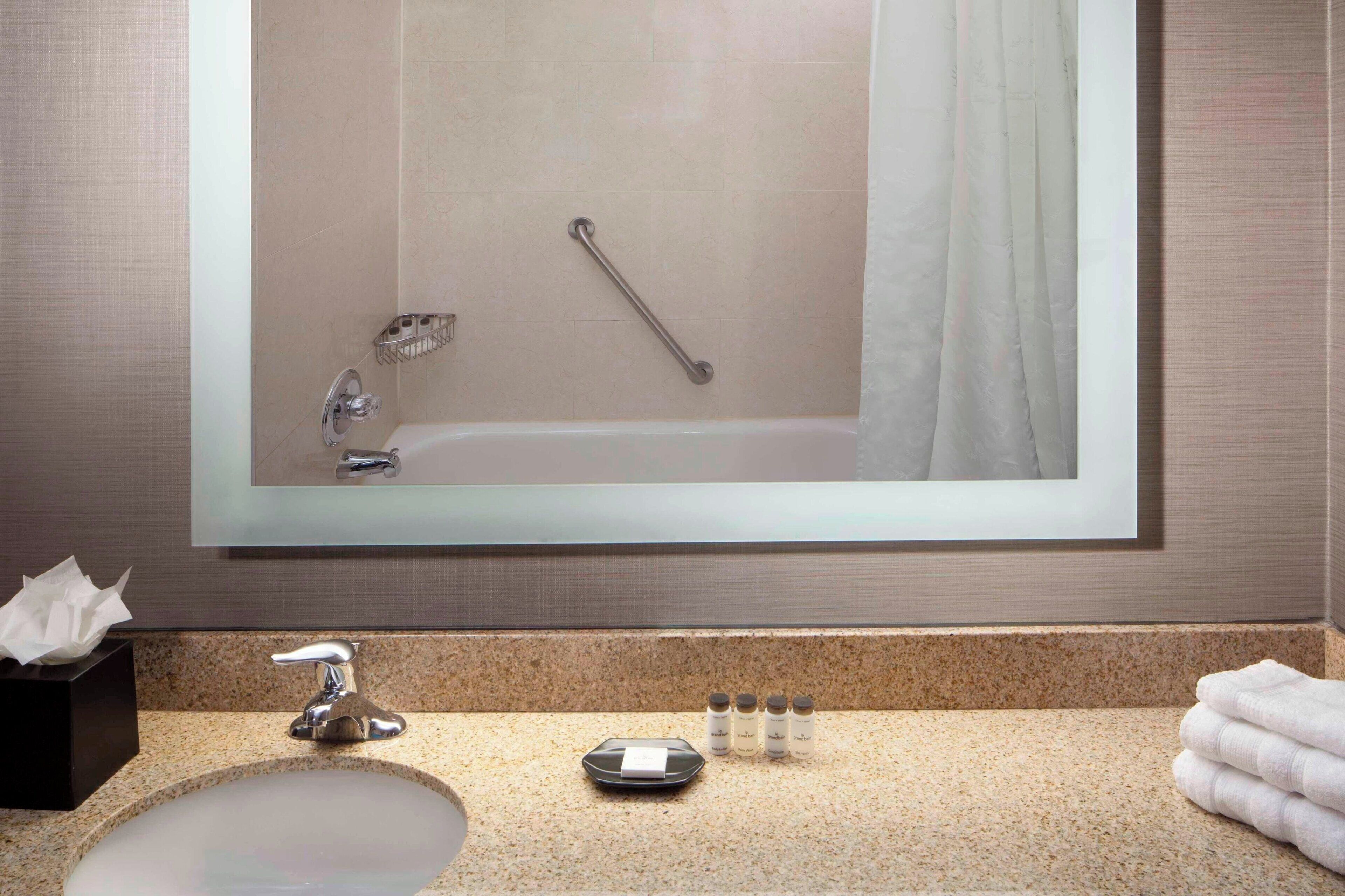 A bathroom with a sink, mirror, and a handrail.