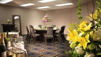 A conference room with a hexagonal patterned carpet, a round table with chairs, a floral centerpiece, and a mirror on the wall.