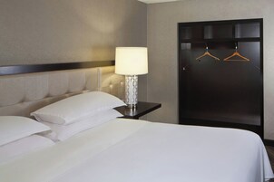 Habitación de hotel con cama, almohadas, mesita de noche con lámpara y armario con perchas.