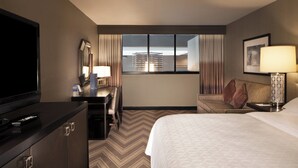 A hotel room with a bed, a desk with a chair, a television, a window with curtains, and a lamp. - Sheraton Bucks County Langhorne (Langhorne)
