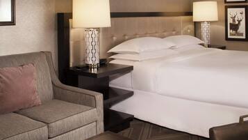 A hotel room with a bed, a sofa, two bedside tables with lamps, and framed pictures on the wall.