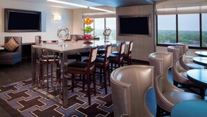 A modern hotel dining area with a long table, multiple chairs, and a view of the cityscape through large windows. - Sheraton Bucks County Langhorne (Langhorne)