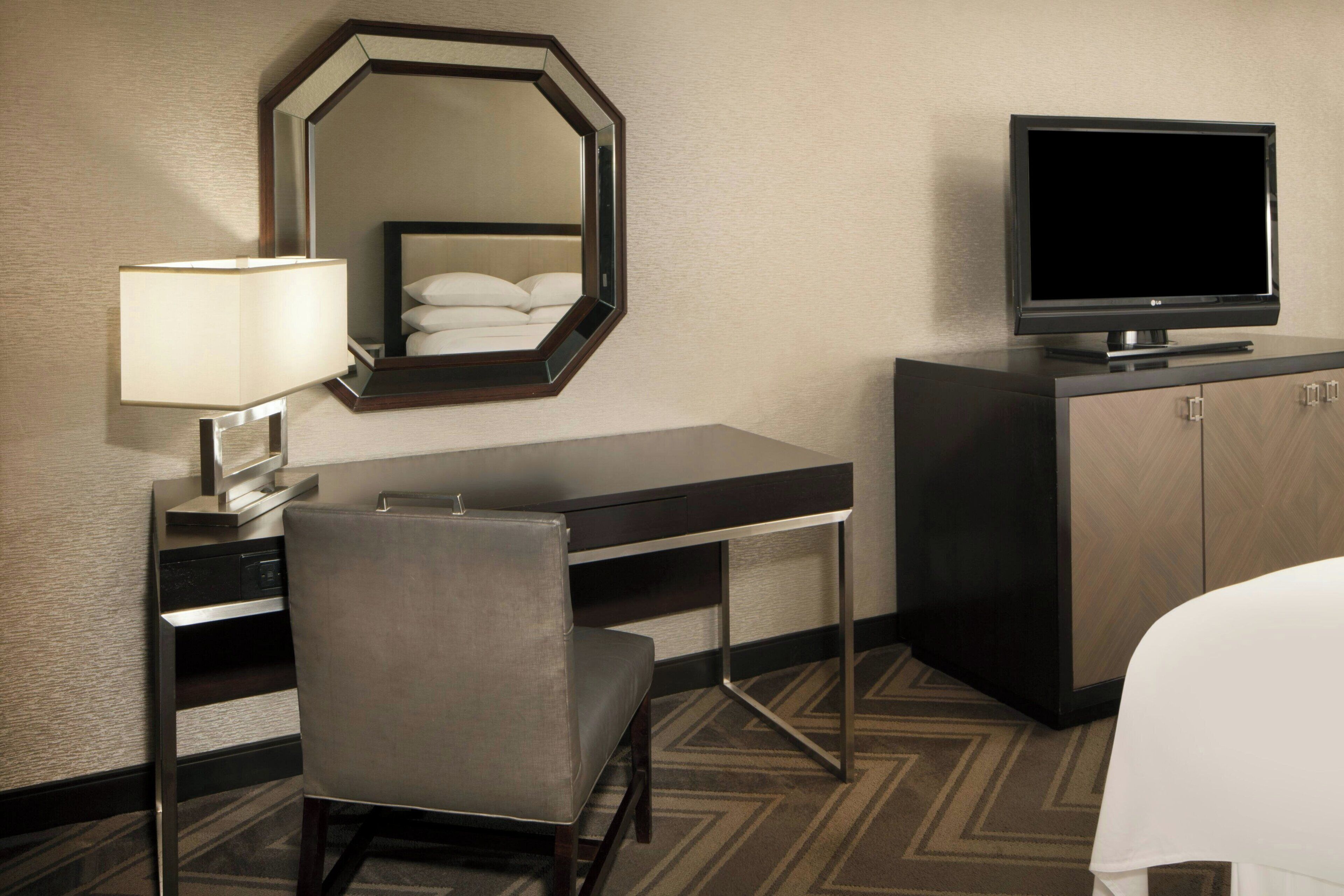 Ein Hotelzimmer mit Bett, Schreibtisch mit Stuhl, Fernseher, Spiegel und Lampe.
