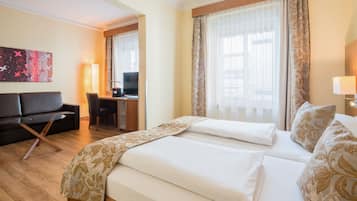 A hotel room with two beds, a desk, a sofa, and a TV.