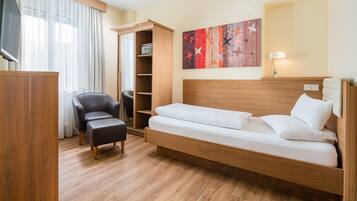 A modern hotel room with a wooden bed, a black leather chair, a wooden wardrobe, and a large window with sheer curtains.
