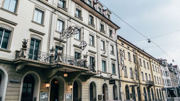 Ein mehrstöckiges Gebäude mit Rundbogenfenstern und Balkonen, mit einem gut sichtbaren Schild mit den Buchstaben „KR“ und „EUZ“.
