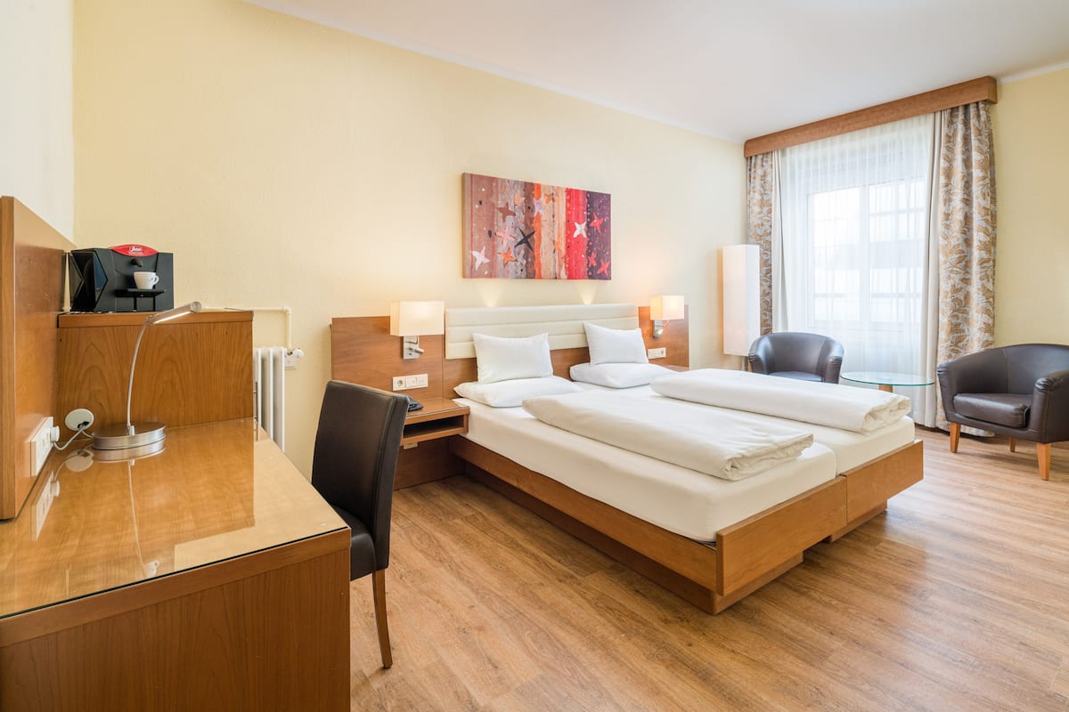 Habitación de hotel con una cama grande, mesitas de noche, un escritorio, una silla y una ventana con cortinas.