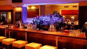 Eine Bar mit einer langen Theke, mehreren Hockern und einer Auswahl an Flaschen und Gläsern.