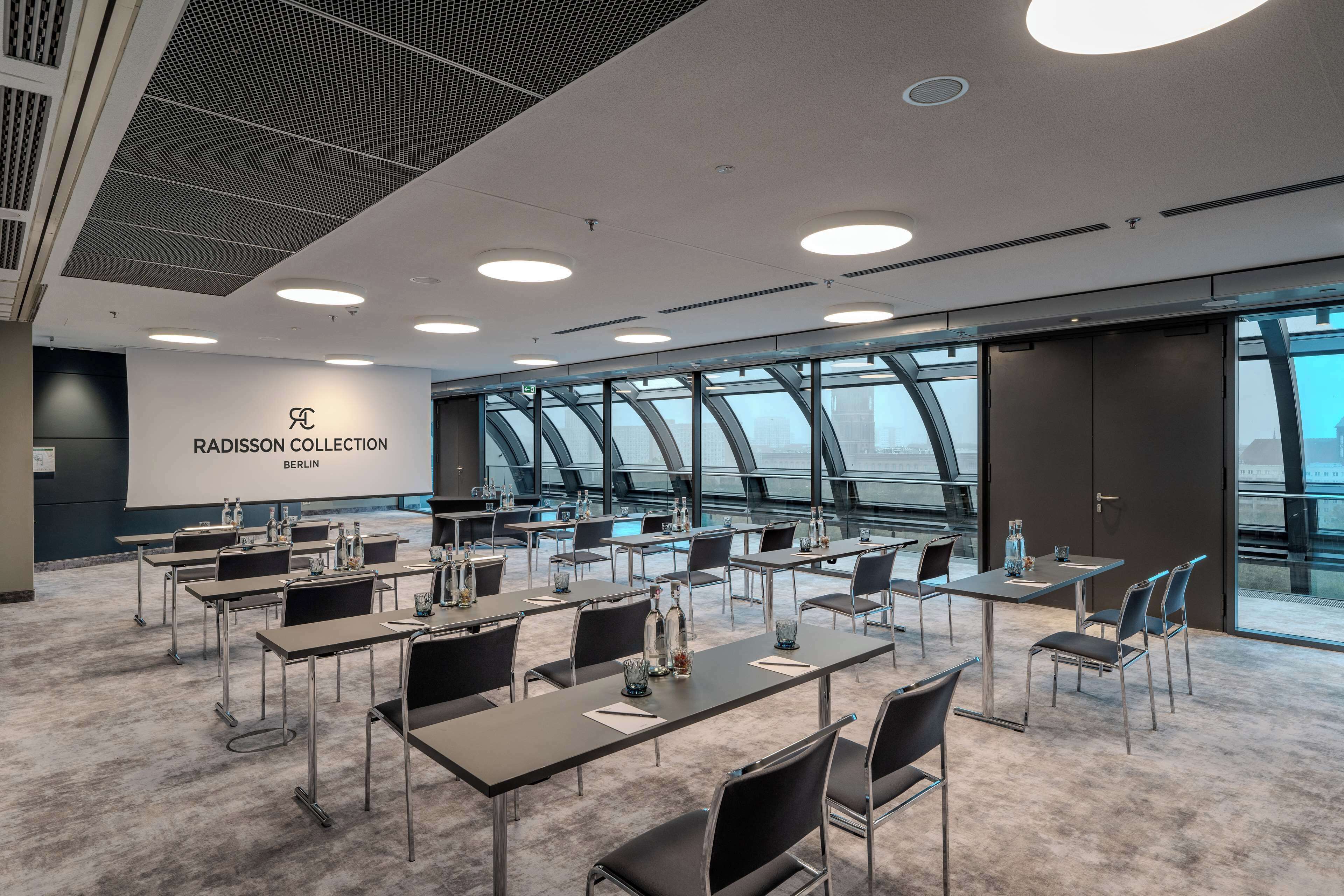 Un salón de conferencias con mesas y sillas, un letrero Radisson Collection y ventanas amplias con vistas.