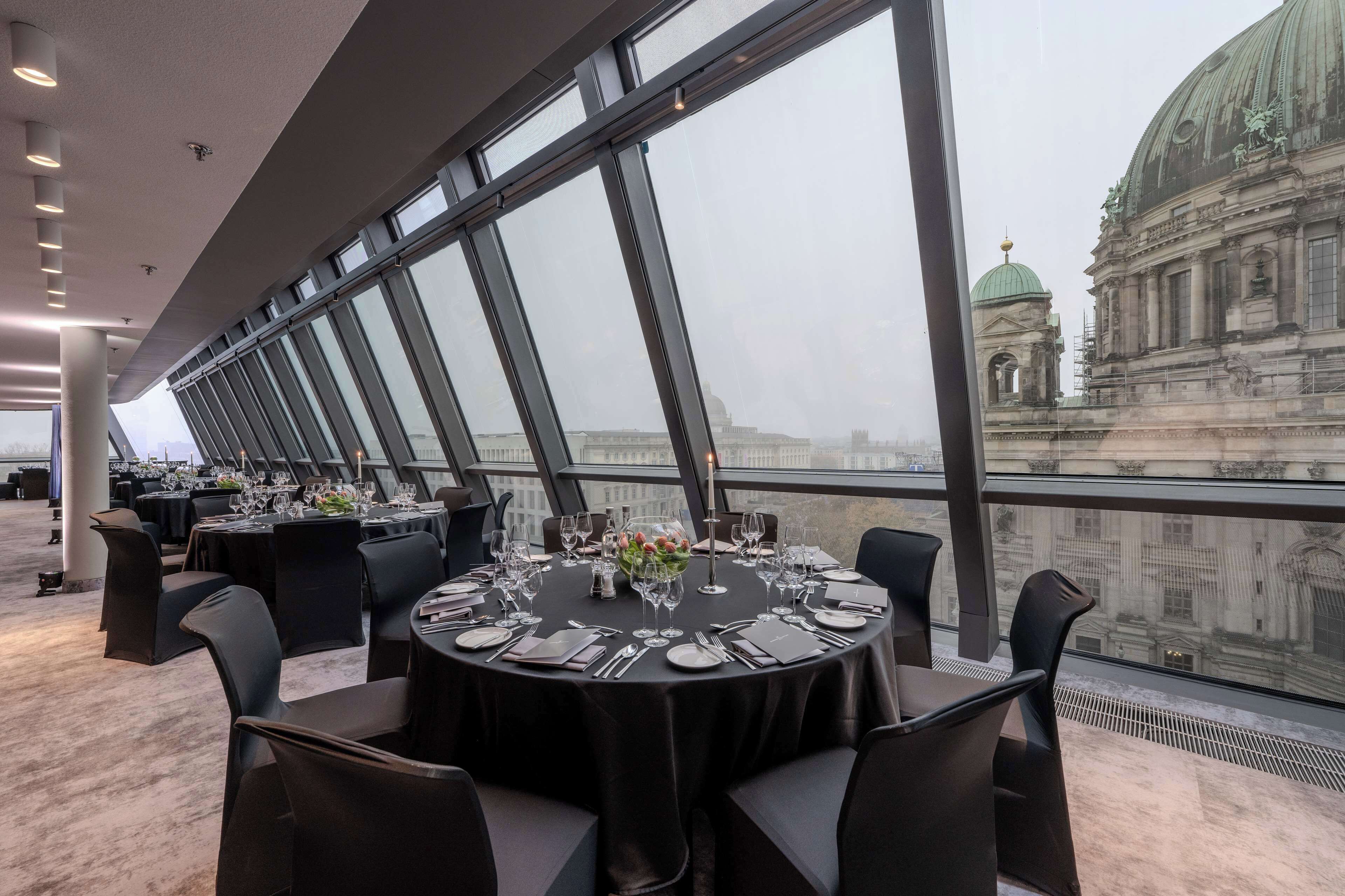 A restaurant with round tables set for dining, large windows offering a view of a historic building.