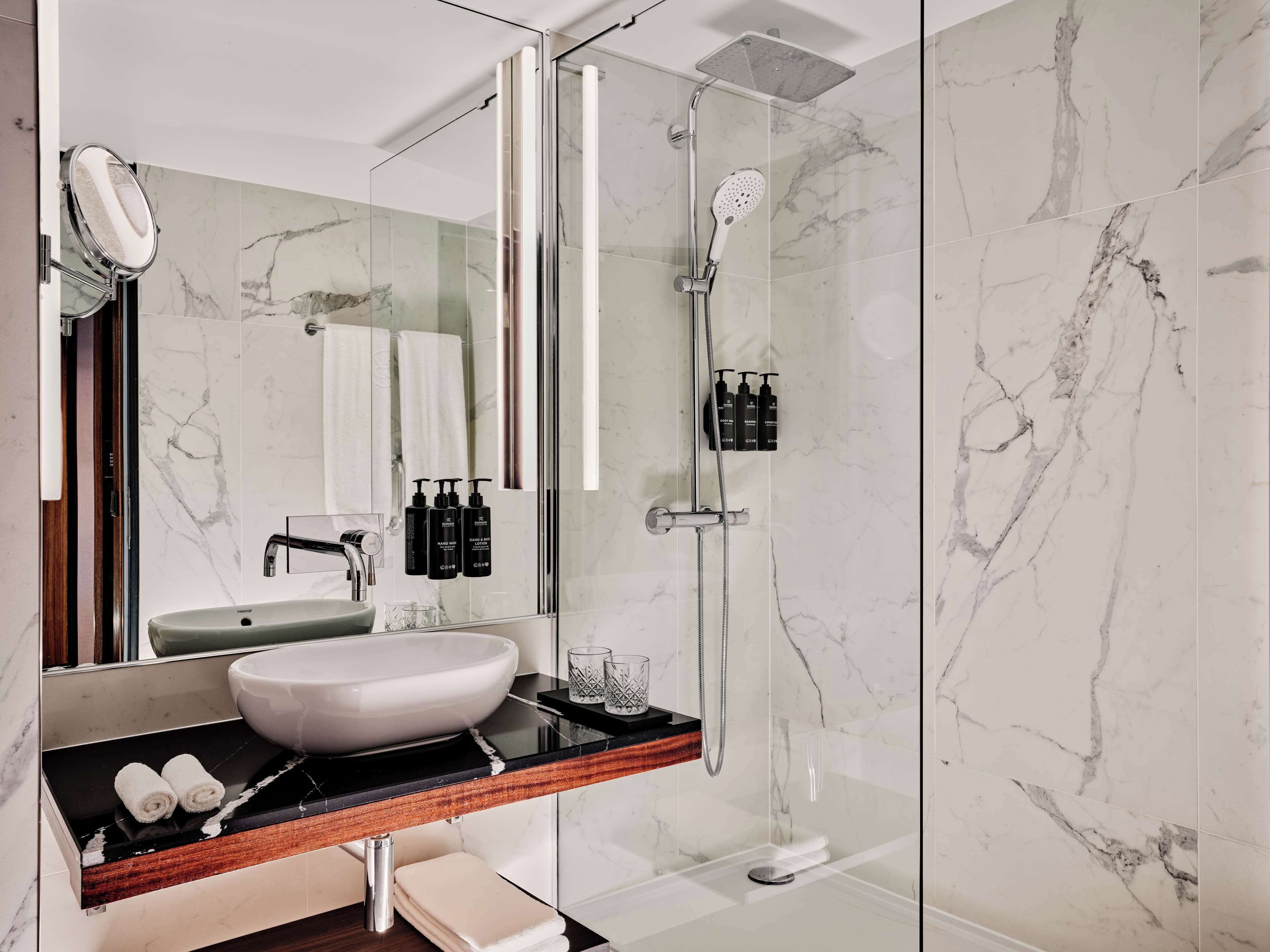A modern bathroom with a large mirror, a white sink, and a glass-enclosed shower area.