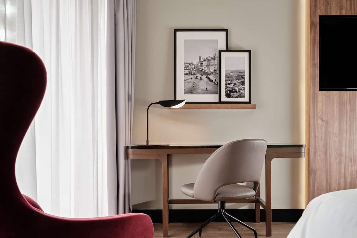 Relax in a serene space with a comfortable bed, a desk for work, and a framed photograph on the wall.