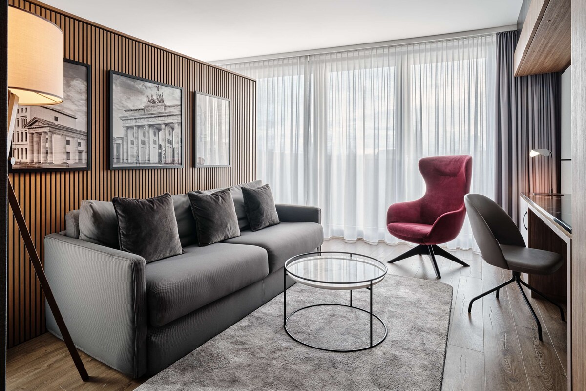 Een moderne woonkamer met een grijze bank, een rode fauteuil, een glazen salontafel en een lamp.