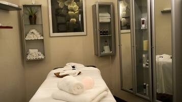 A neatly arranged room with a massage table, towels, a potted plant, and a glass cabinet with toiletries.
