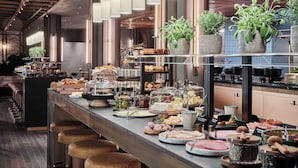 A buffet setup with various food items, including meats, cheeses, and pastries, arranged on a long counter with stools for seating.