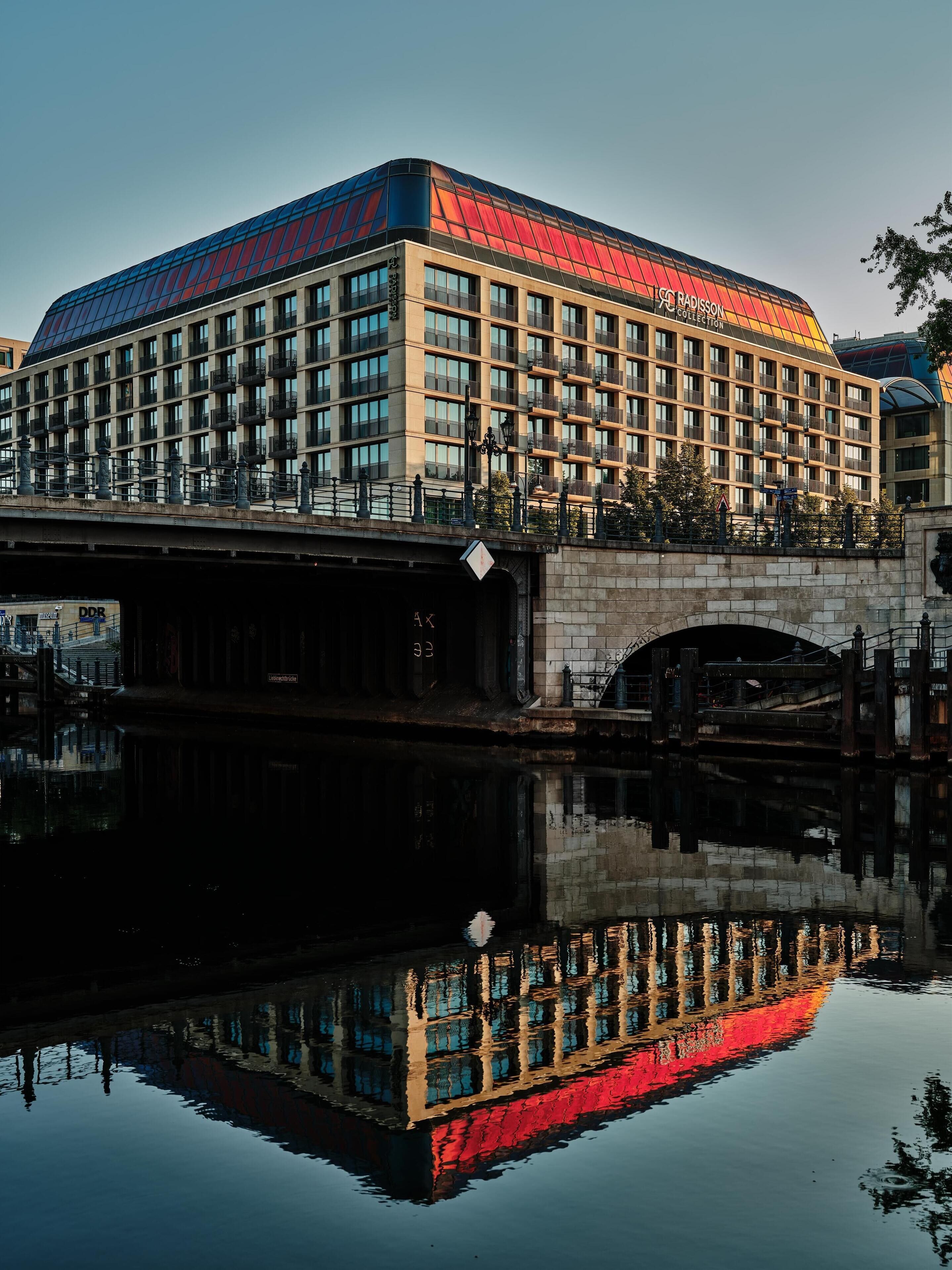 Un hotel moderno con fachada de vidrio y balcones, reflejado en el agua.