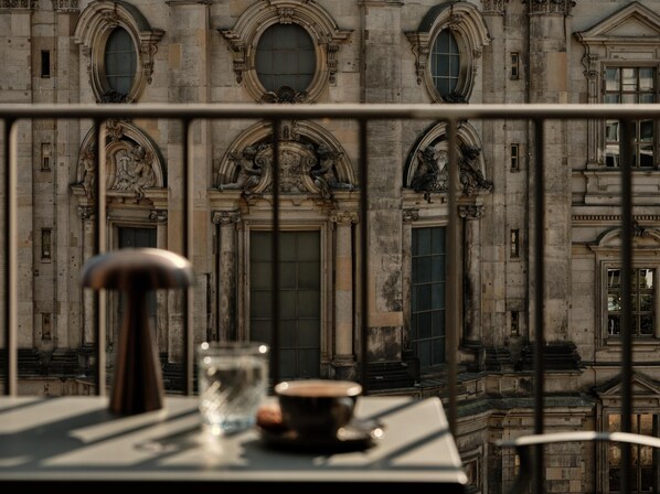 A balcony with a table, a glass, and a cup. The background features a historic building with ornate architecture.