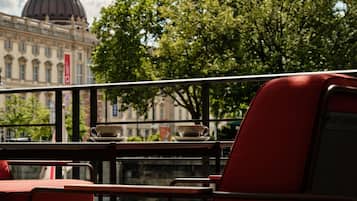 Un café con sillas y mesas rojas, vista de un edificio con cúpula y árboles al fondo.