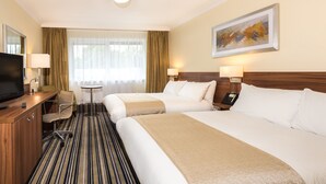 A hotel room with two beds, a desk with a TV, a chair, a small table, and a painting on the wall. - Holiday Inn Warrington by IHG (Warrington)