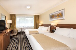A hotel room with two beds, a desk with a TV, a chair, a small table, and a painting on the wall.
