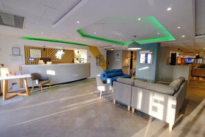A hotel lobby with a reception desk, seating area, and a television screen. - Holiday Inn Warrington by IHG (Warrington)