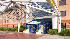 A Holiday Inn with a covered entrance, glass doors, and a brick building in the background. - Holiday Inn Warrington by IHG (Warrington)