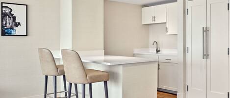 A modern kitchen with a central island, two bar stools, white cabinetry, and a refrigerator.
