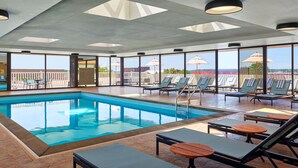 Un área de piscina con tumbonas y sombrillas, ventanas amplias y vistas al cielo.