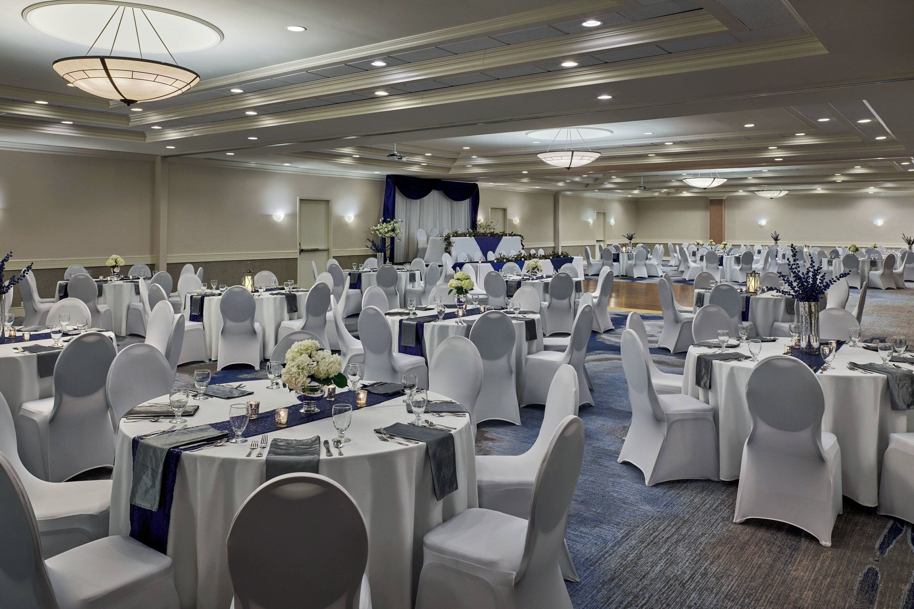 Une salle de banquet avec des tables rondes, des chaises blanches et des rideaux bleus.