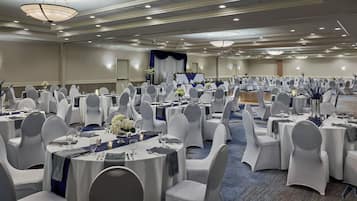 Une salle de banquet avec des tables rondes, des chaises blanches et des rideaux bleus.