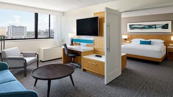 Una habitación de hotel con cama, escritorio, silla, televisor y vista a la ciudad.