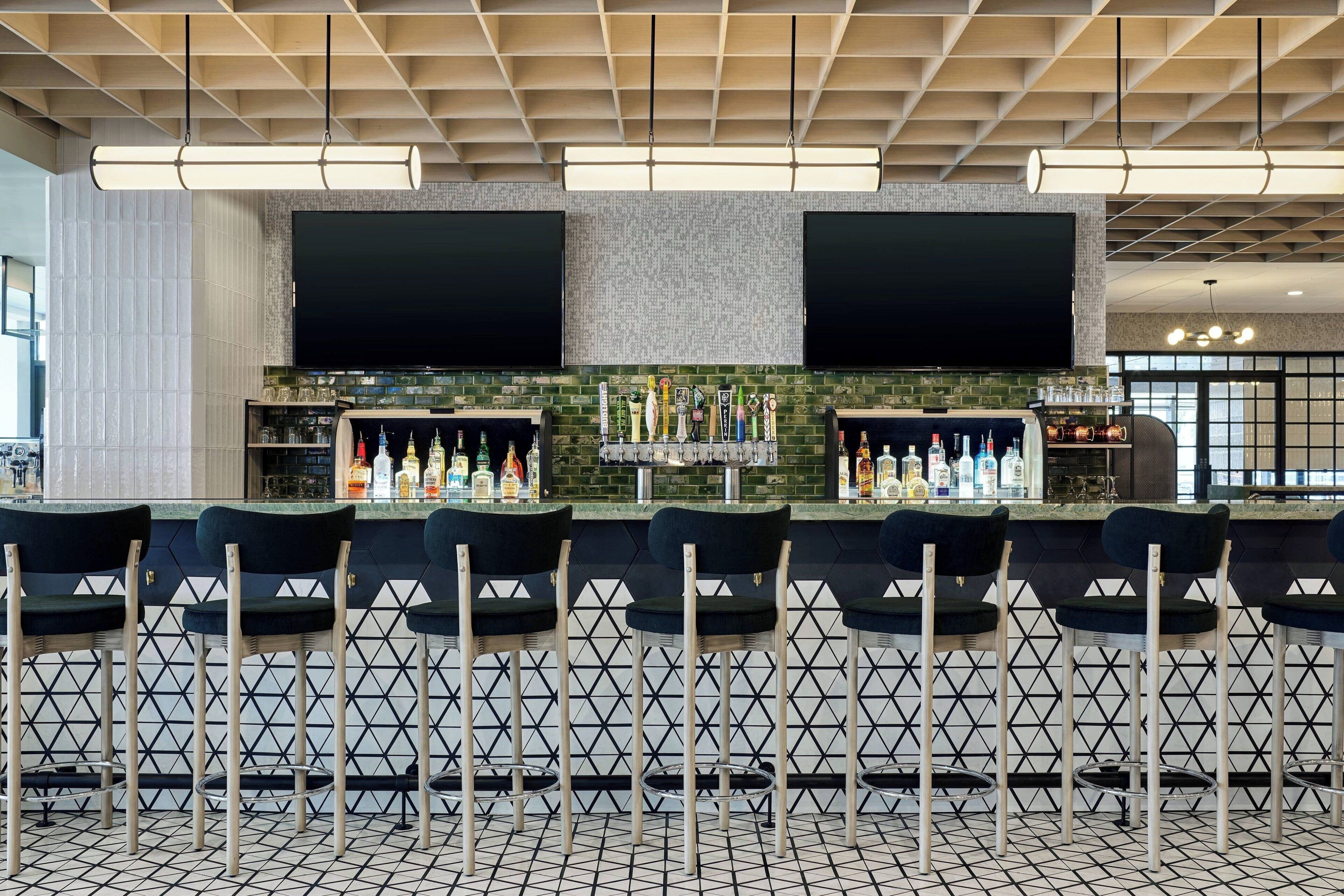 A bar area with a modern design, featuring a black and white patterned floor, a counter with a green tiled backsplash, and multiple bar stools.