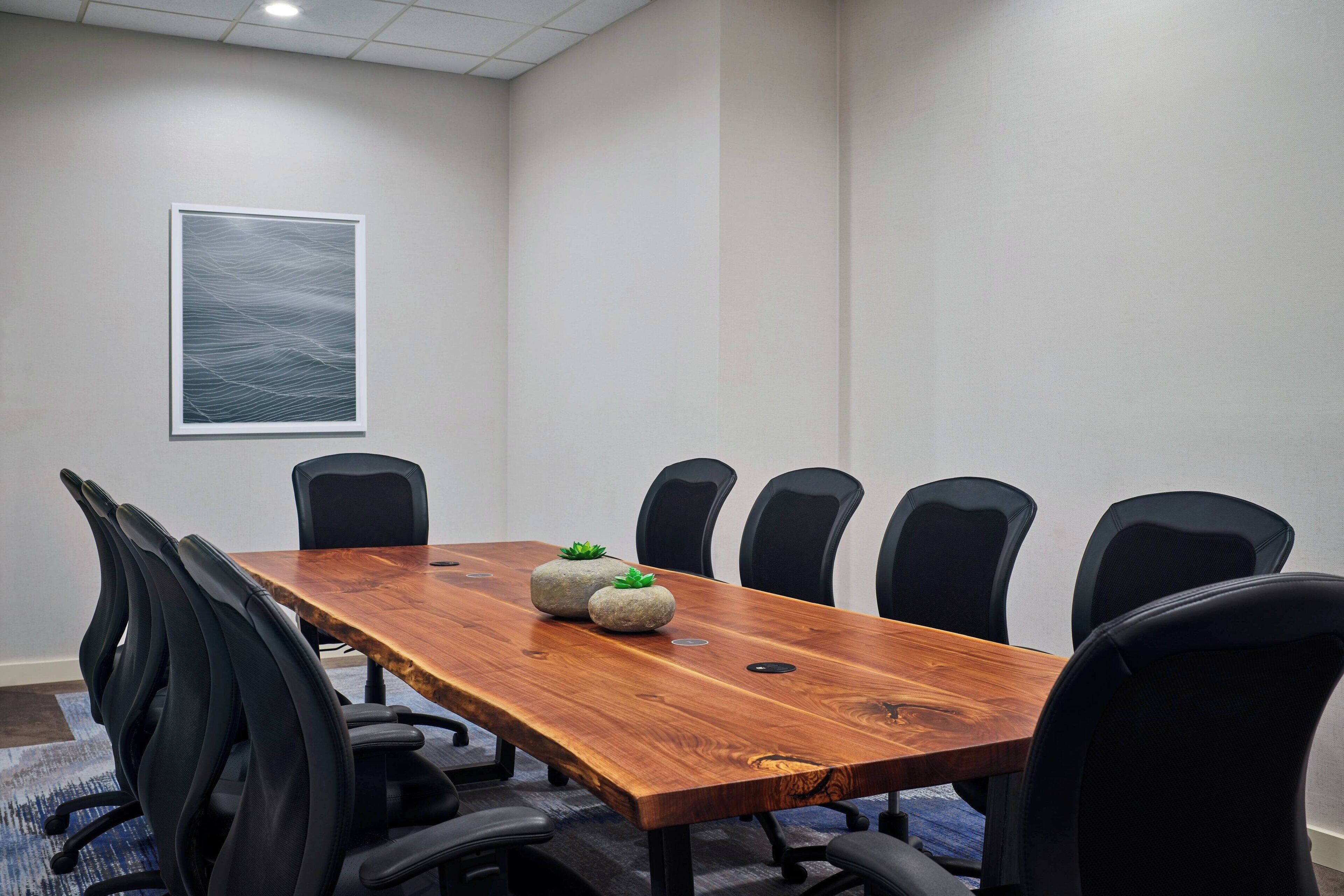 A conference room with a wooden table, black chairs, and a framed abstract artwork on the wall.