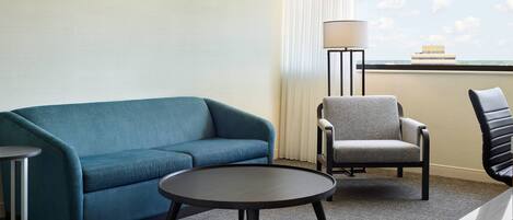 Ein Hotelzimmer mit einem blauen Sofa, einem grauen Sessel, einem kleinen runden Tisch und einer Lampe.