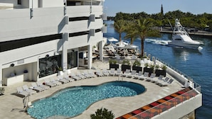 Un hôtel moderne doté d’une piscine, d’un espace extérieur aménagé et offrant une vue sur un yacht amarré.