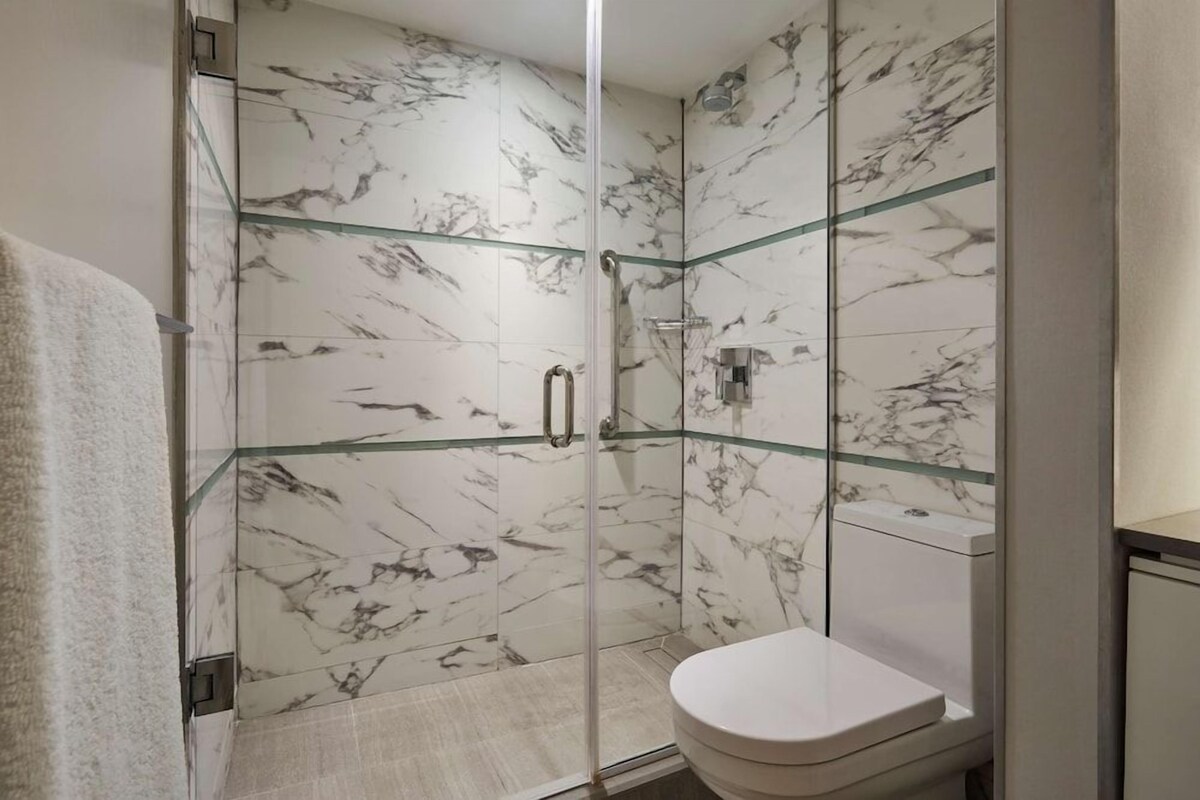 A bathroom with a glass-enclosed shower, marble walls, and a white toilet.
