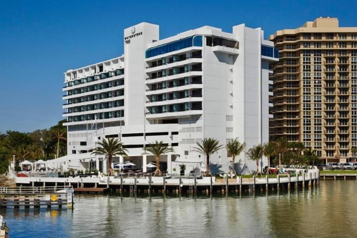A multi-story hotel with a white facade, located near a body of water with a dock.