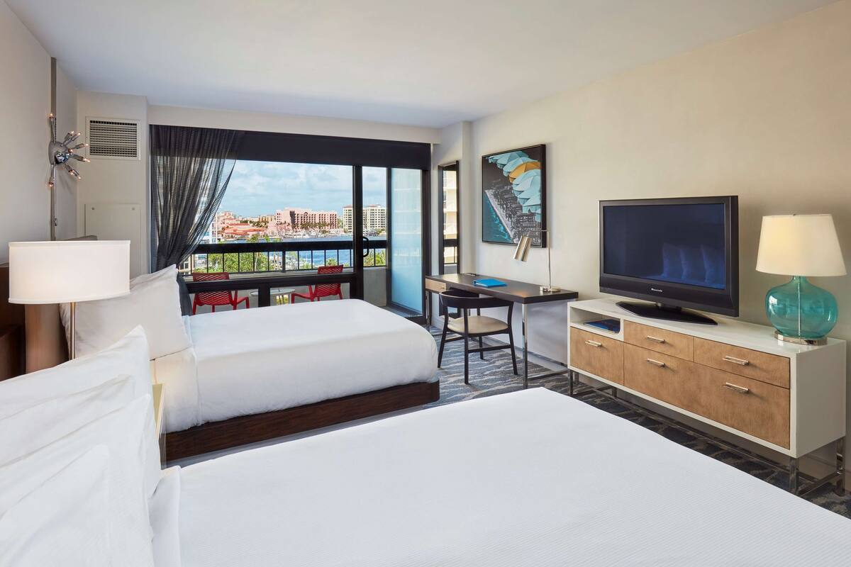 A hotel room with a bed, desk, TV, and a view of the city.