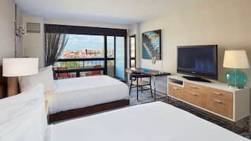 A hotel room with a bed, desk, TV, and a view of the city.