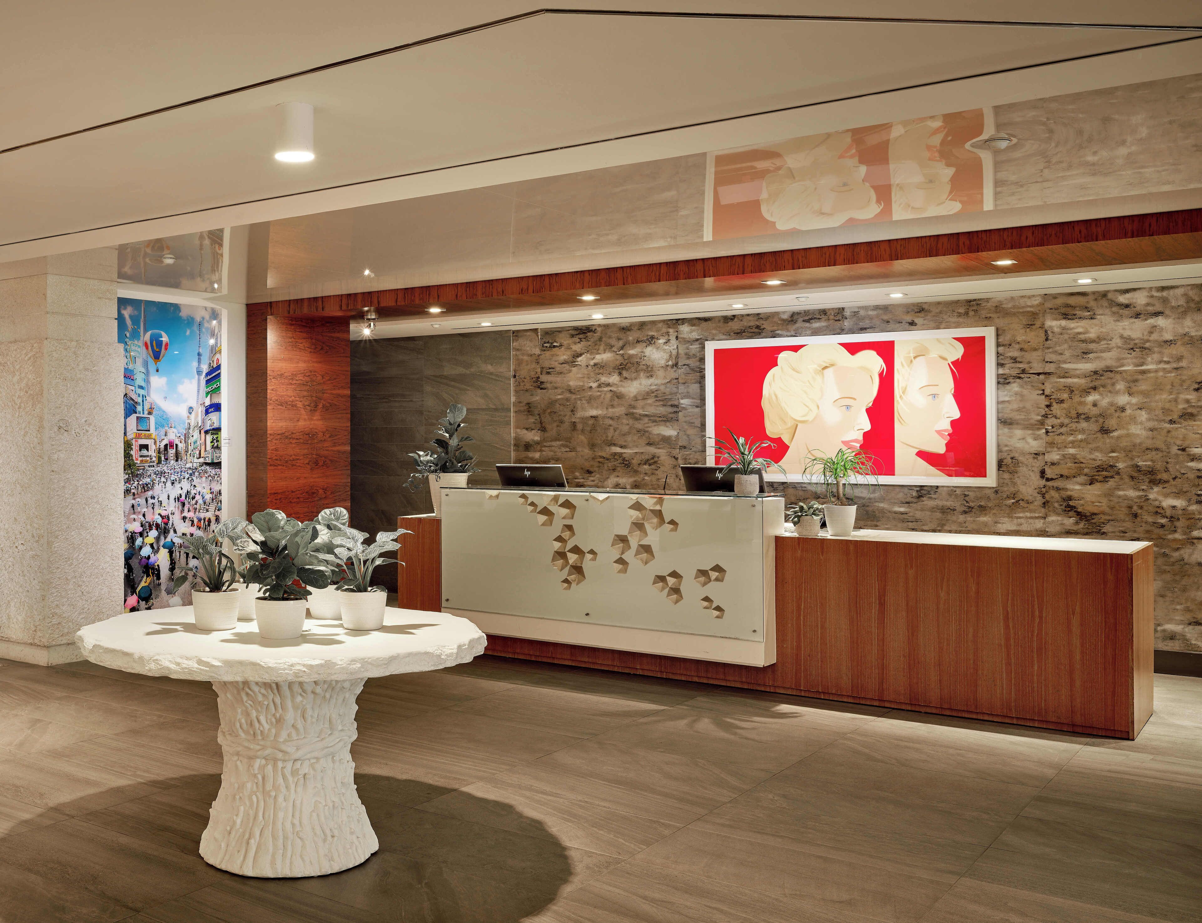 A reception area with a wooden reception desk, a large abstract painting, and a round table with potted plants.