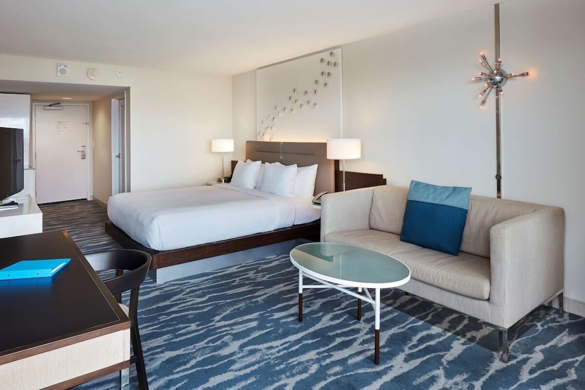A hotel room with a bed, a sofa, a coffee table, and a desk with a chair.